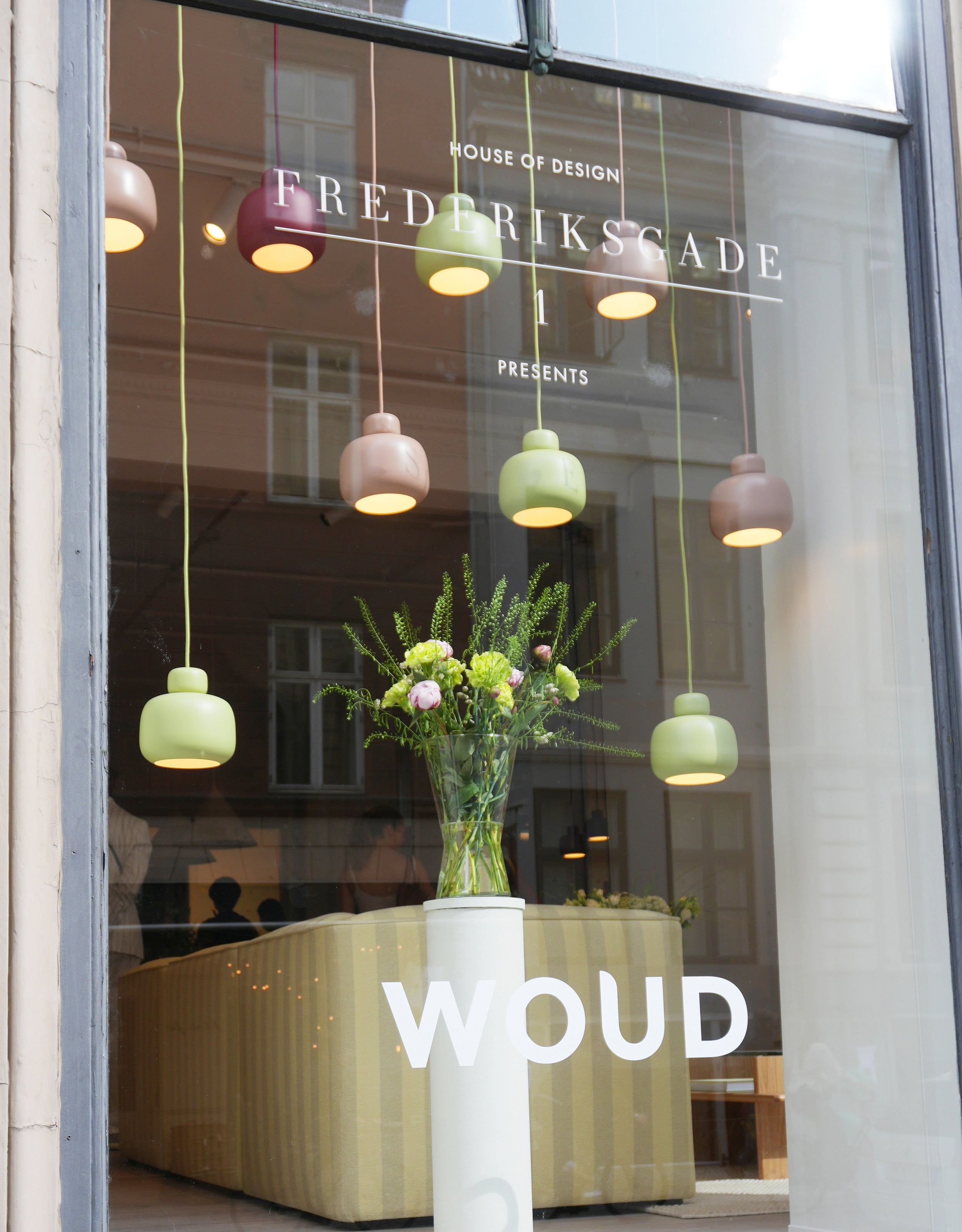Cluster of colorful Scandinavian pendants seen through a window from outside.