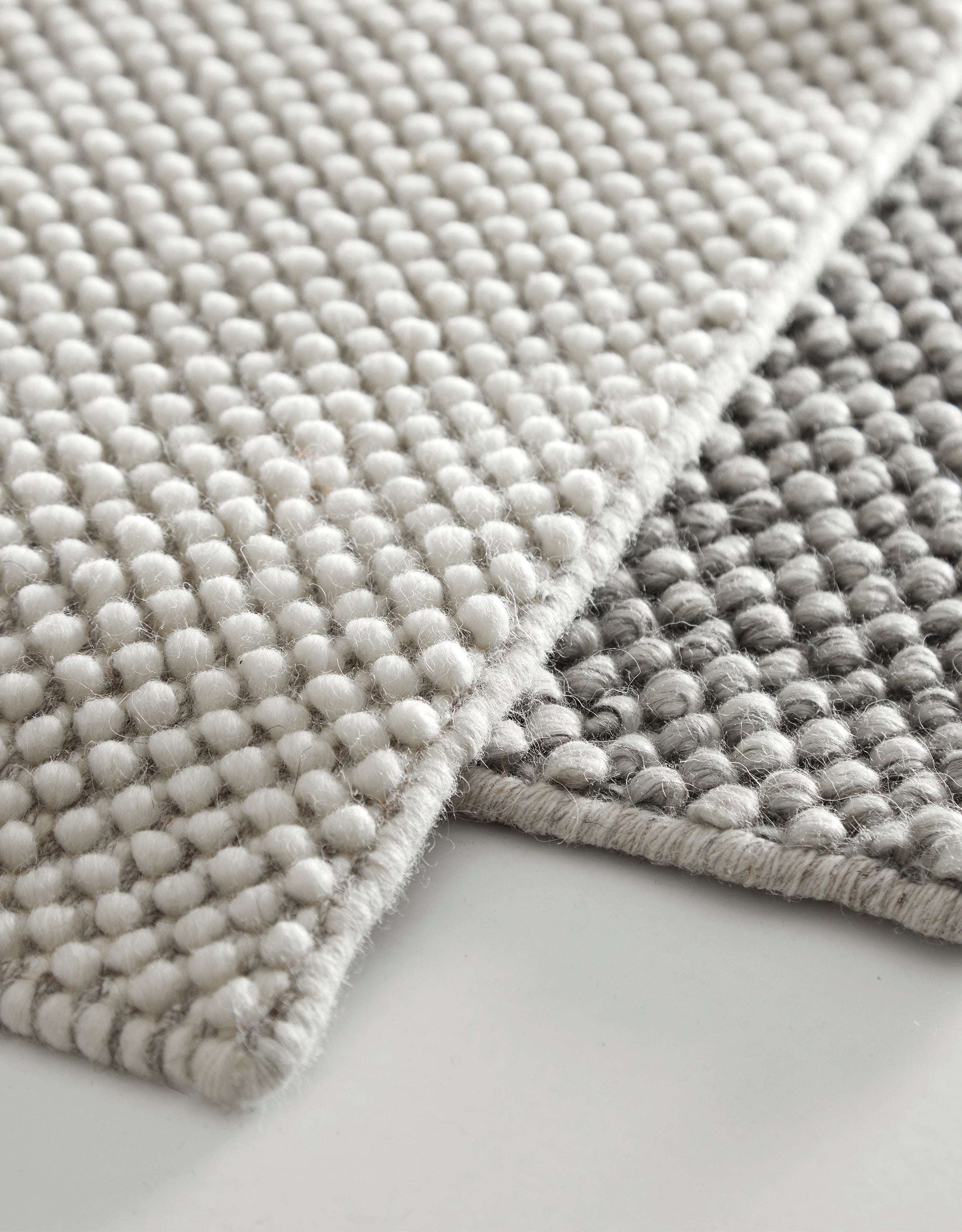 Close-up of two handwoven rugs with small circular droplets in off-white and dark grey