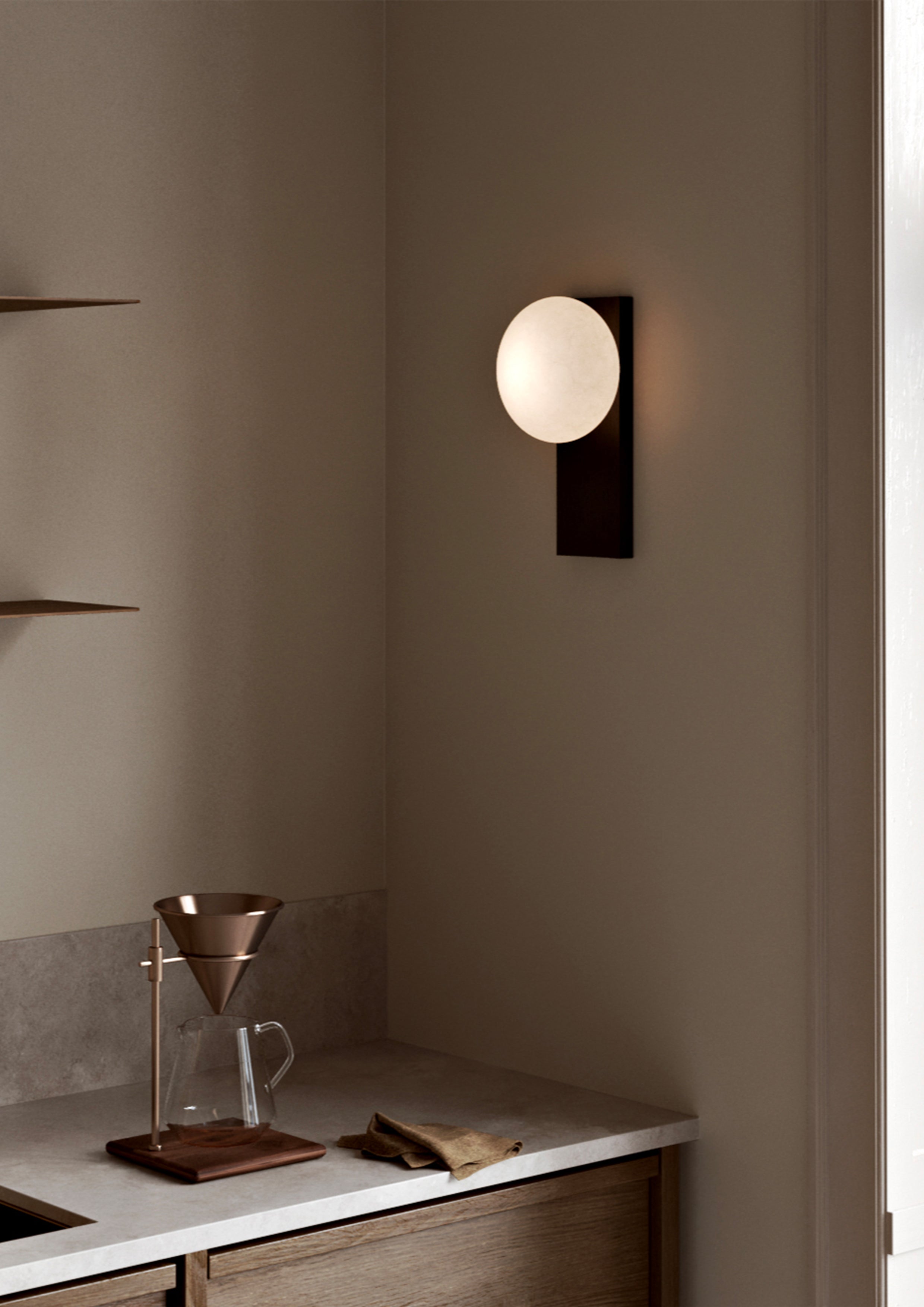 Wall lamp in black painted ash with opal glass shade over kitchen countertop.