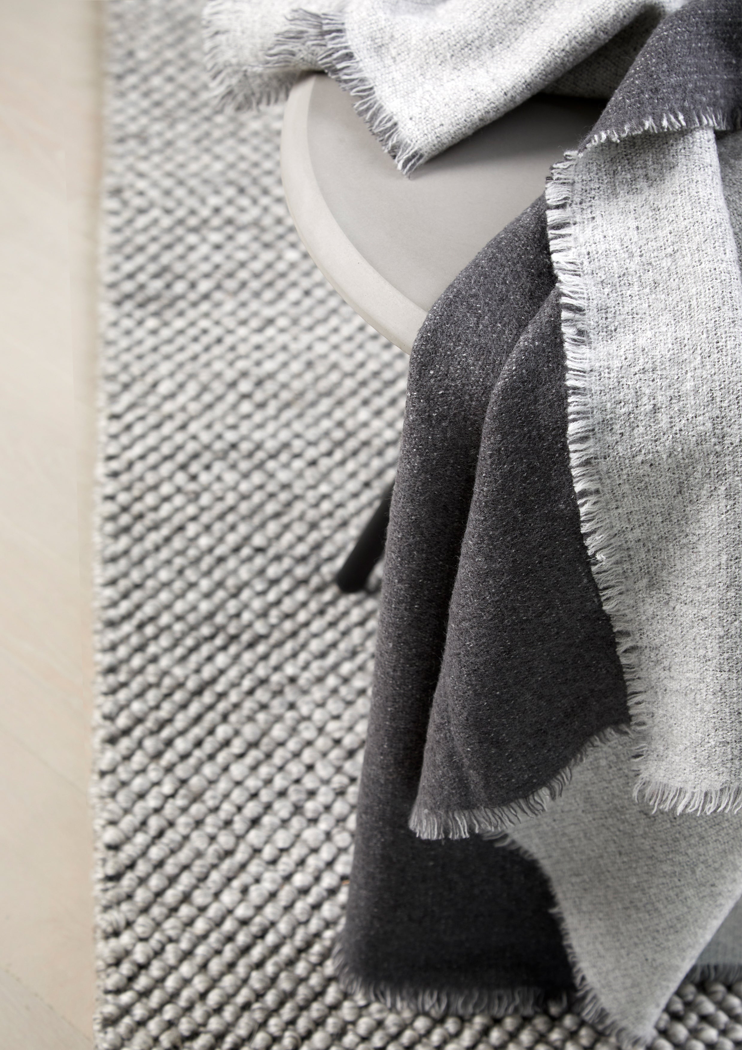 Light grey and dark grey woven plaid in a two-tone design, laid on a table with a grey handwoven rug underneath.