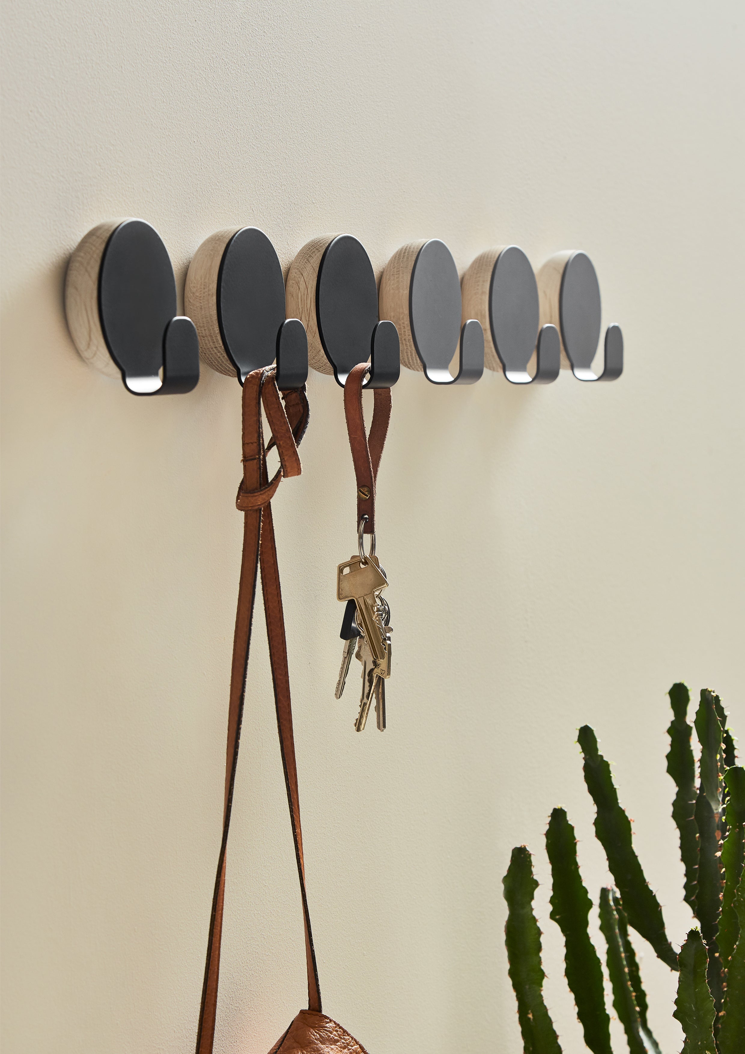Round oak and metal hooks hanging in a row, one with a key cord, one with a bag.
