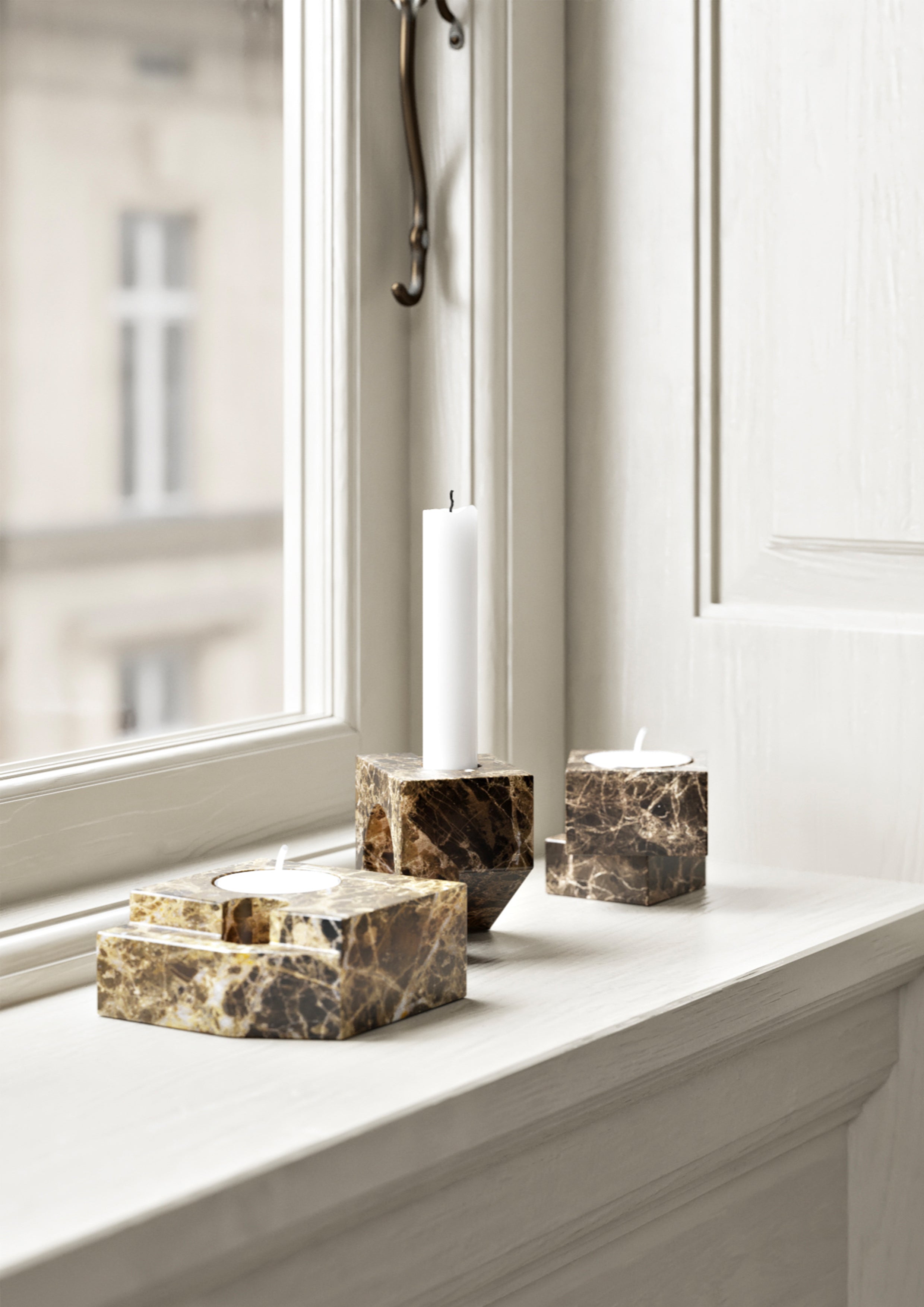Three small candle holders in brown solid marble on a windowsill.
