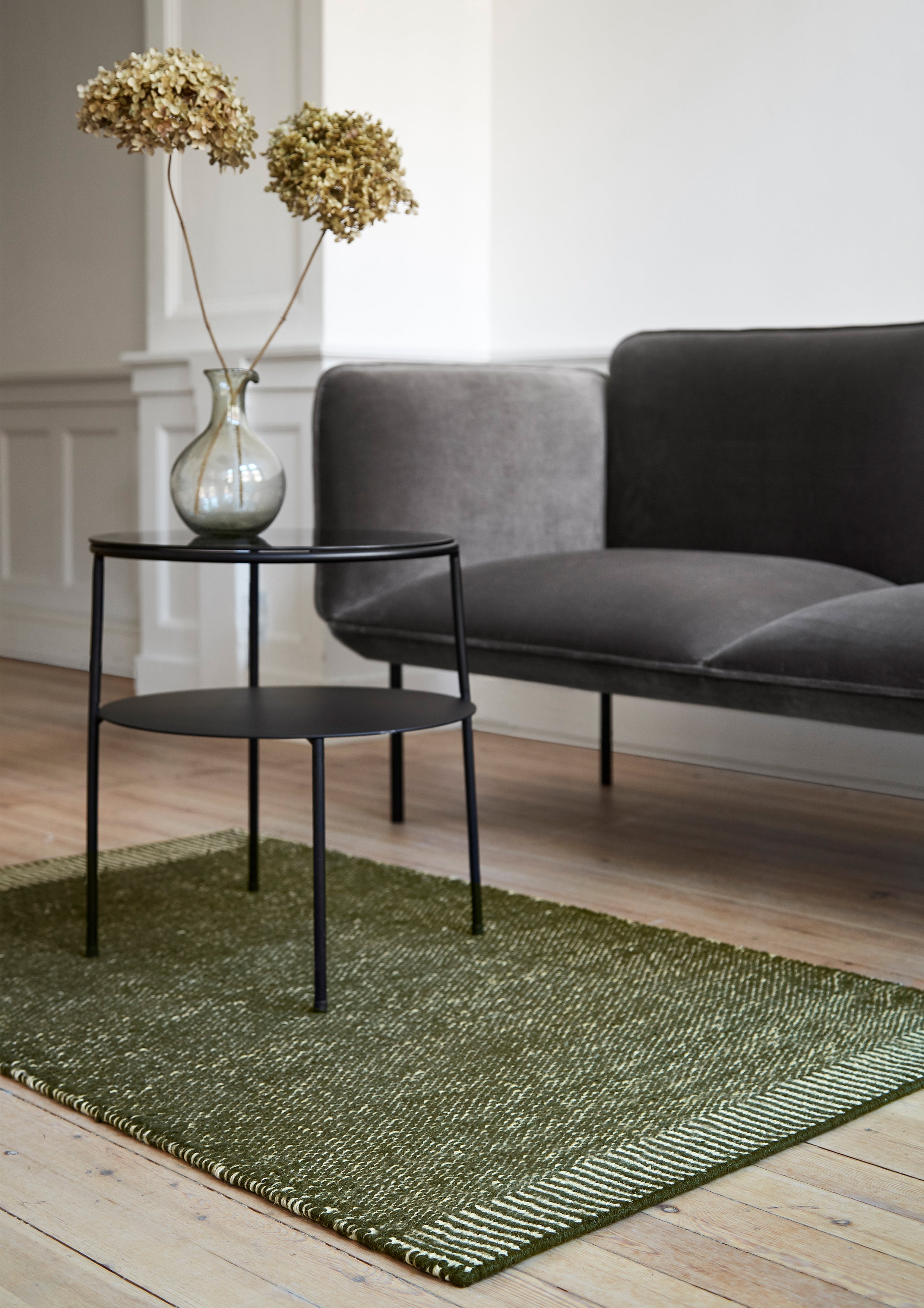 Black side table in front of minimalist sofa on green handwoven rug.