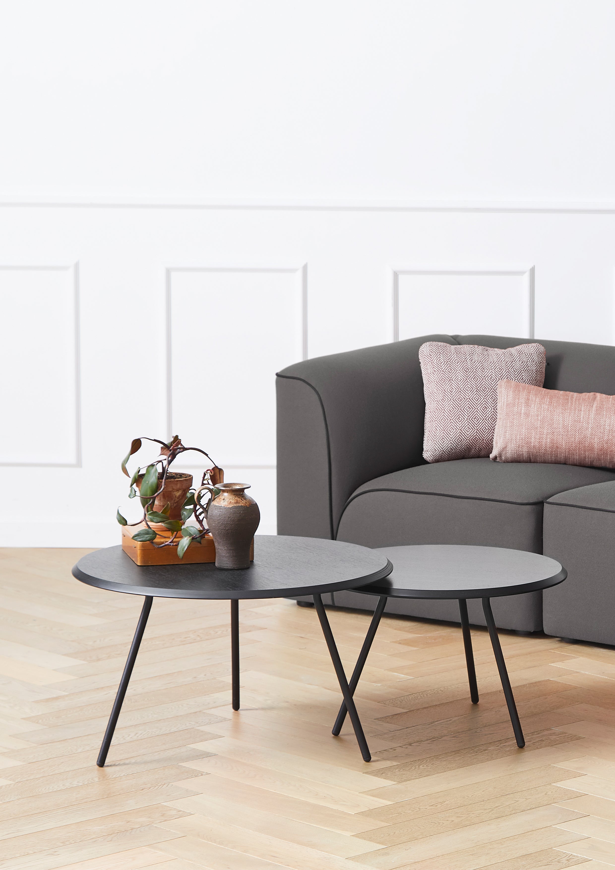 Minimalist round coffee tables in black ash with black metal legs, different heights, placed in front of sofa.