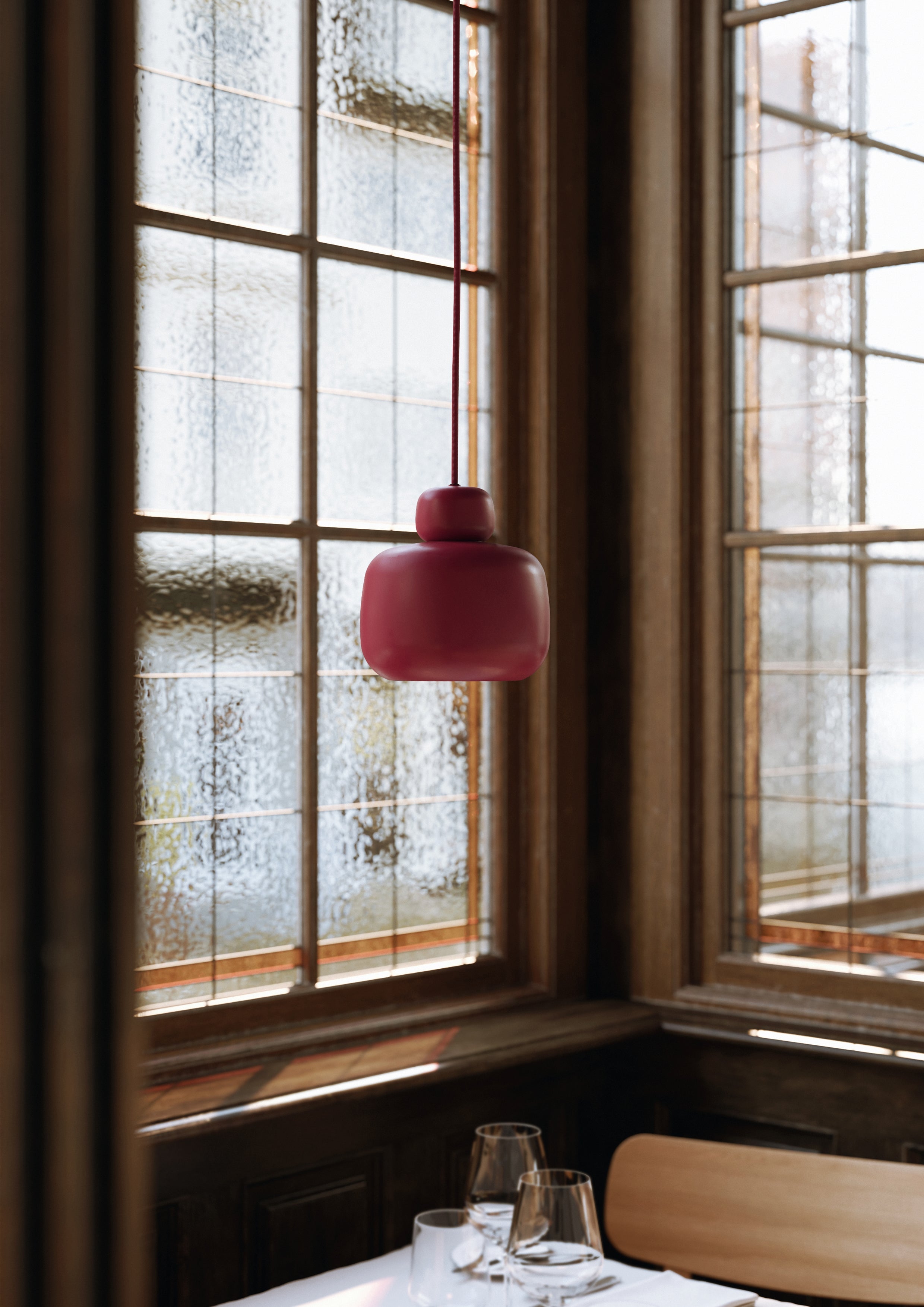 Deep red painted metal pendant in Scandinavian design above restaurant table with paned windows in the background.
