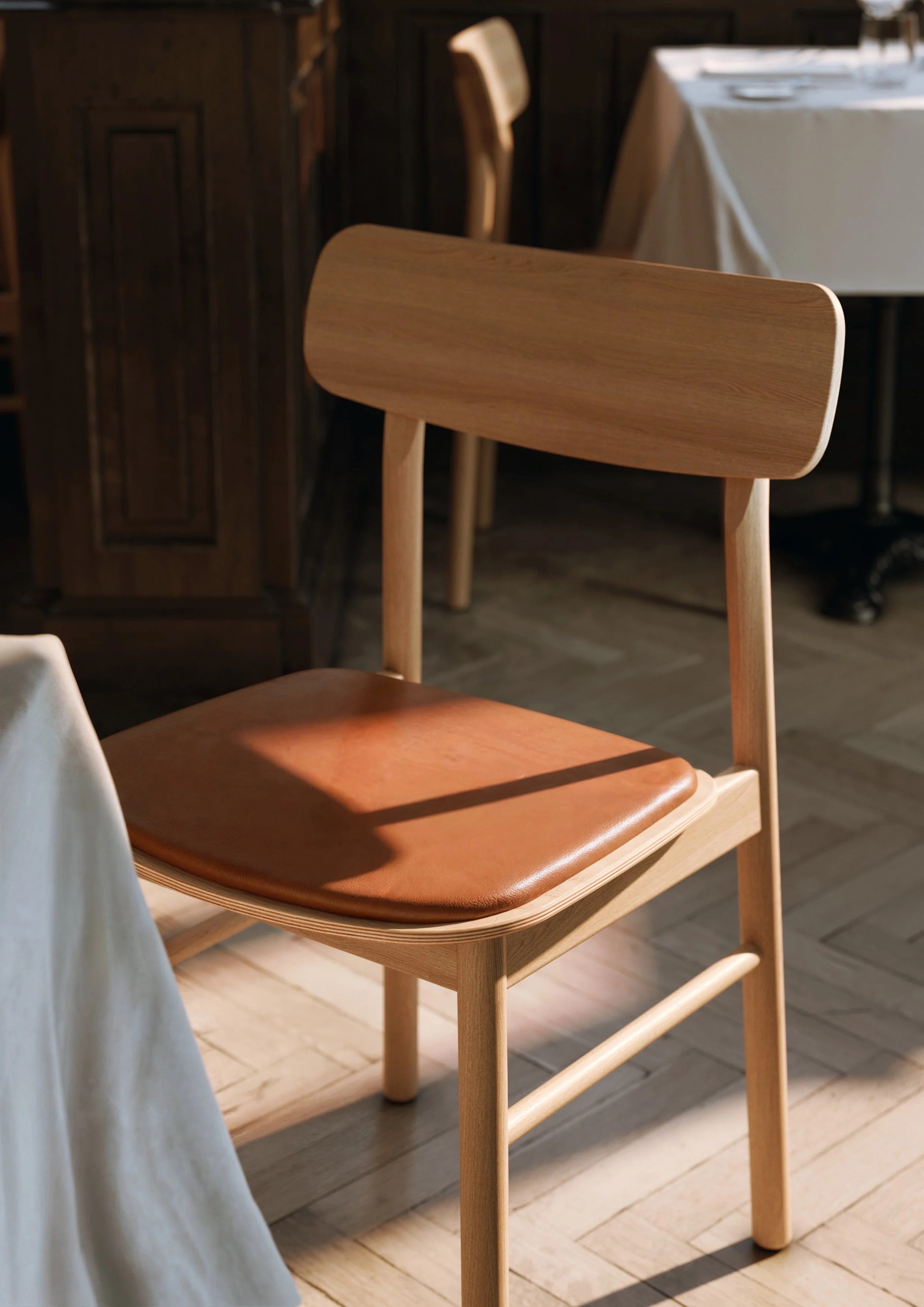 Oiled oak dining chair with cognac leather seat in restaurant with natural sunlight.