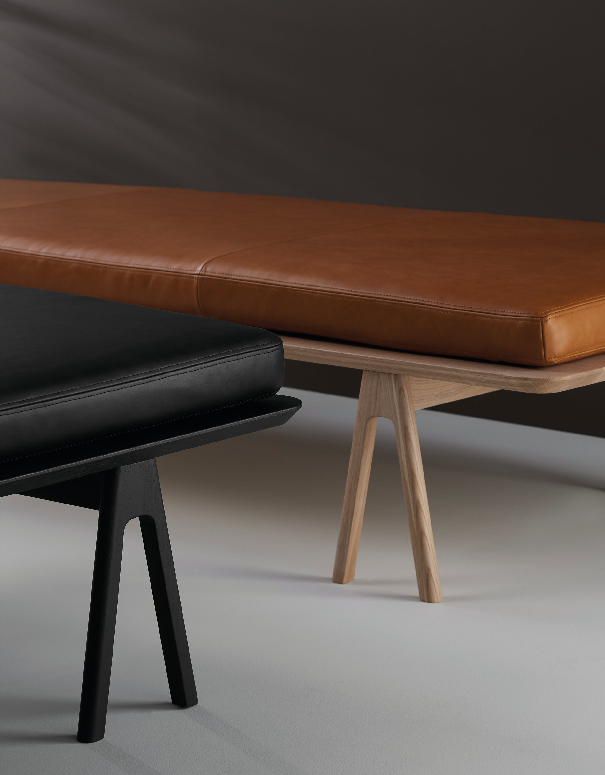 Close-up of two daybeds, one in oak with a cognac leather mattress and one in black with a black leather mattress